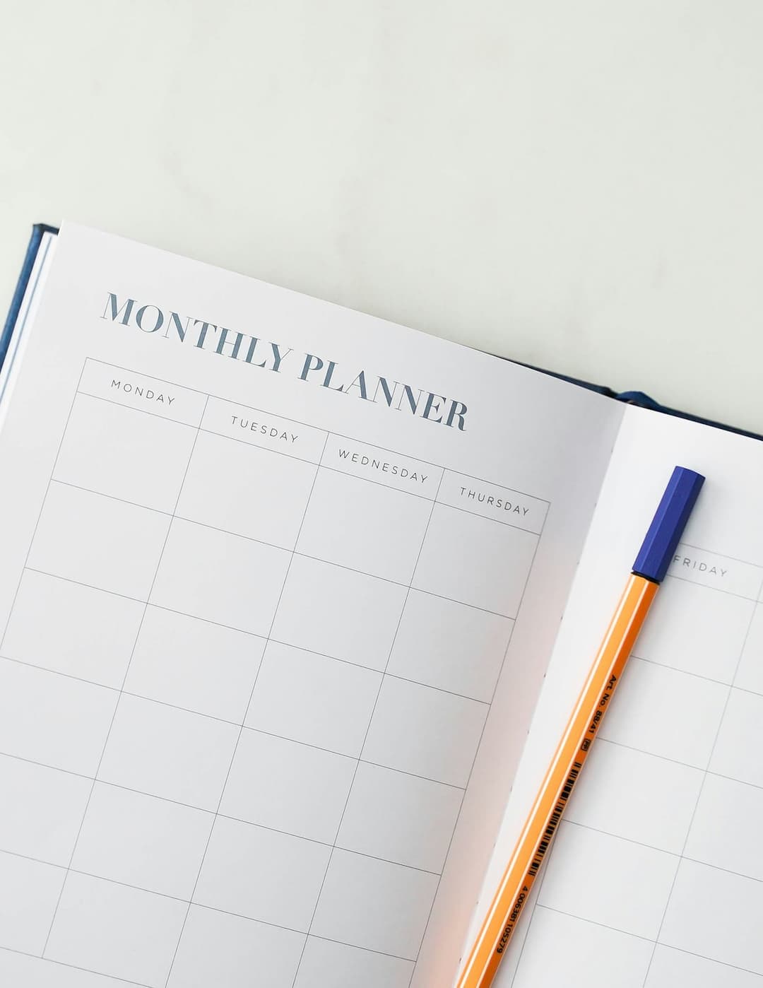 A laptop next to an open notebook and a monthly planner